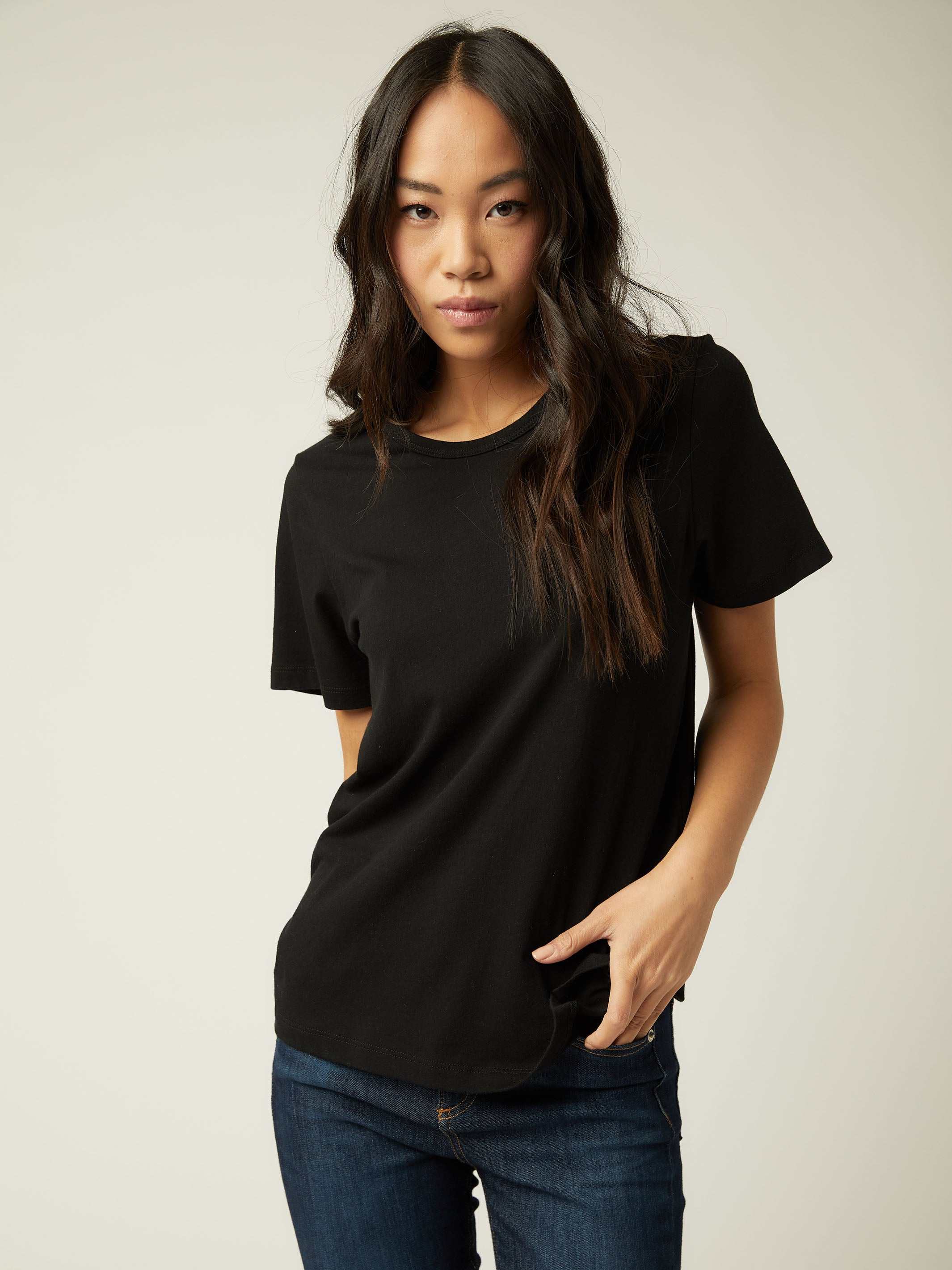 Woman wearing black basic short sleeve tee with crew neck and straight hem paired with blue jeans