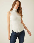 Woman wearing a slim fit sleeveless turtleneck rib-knit top with shirttail hem and dark jeans
