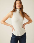 Woman wearing a slim fit sleeveless turtleneck rib-knit top in light gray with shirttail hem.