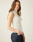 Woman wearing a slim fit sleeveless turtleneck rib-knit top with shirttail hem in light beige