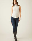 Woman wearing a slim-fit sleeveless turtleneck top paired with dark jeans and black boots