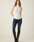 Woman wearing a slim fit sleeveless turtleneck knit top paired with dark jeans and black boots