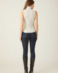 Woman wearing a slim fit sleeveless turtleneck top paired with dark jeans and black boots, back view