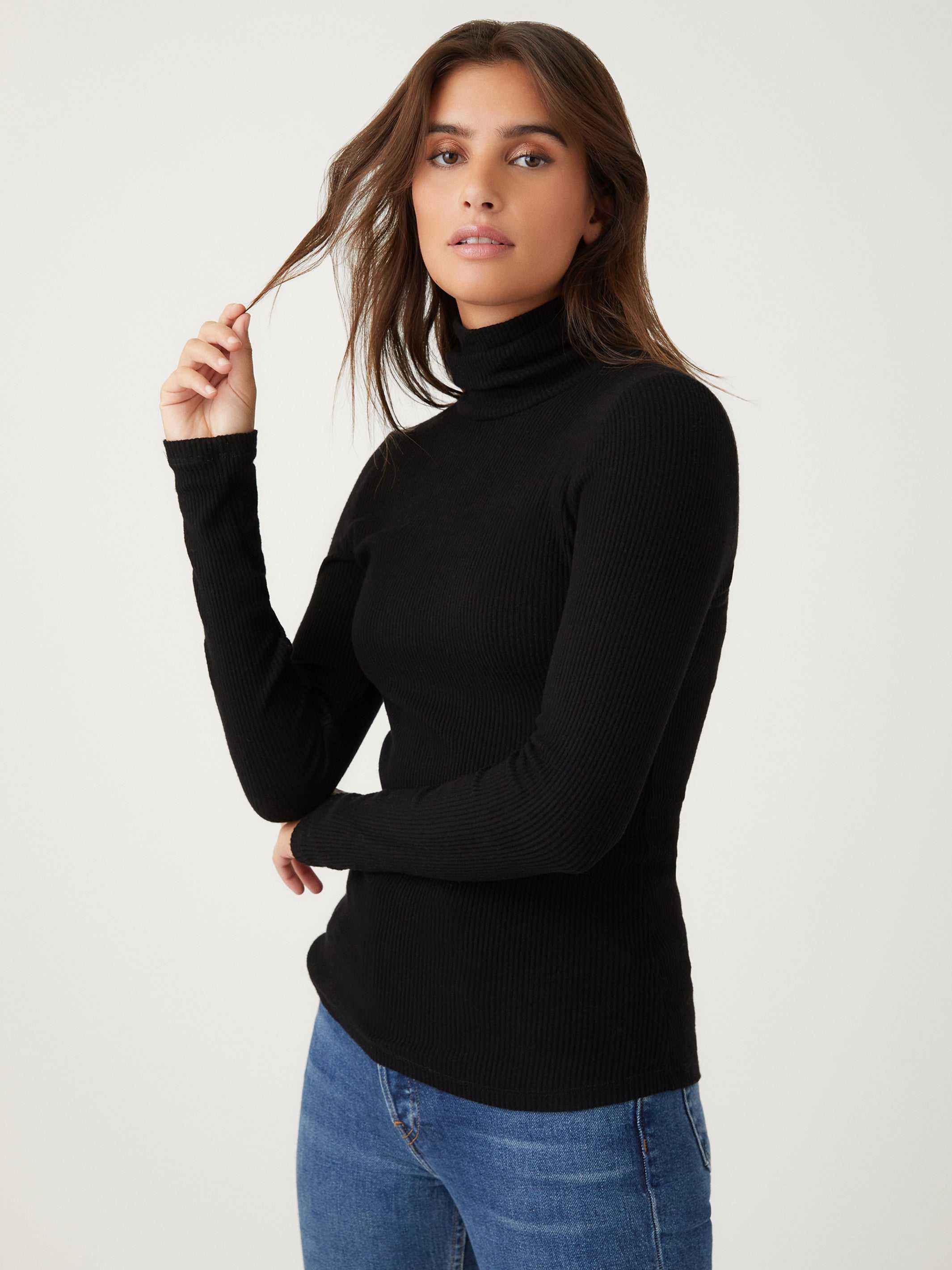 Woman wearing a black long sleeve turtleneck rib-knit top paired with blue jeans