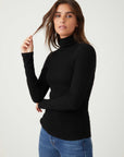 Woman wearing a black long sleeve turtleneck rib-knit top paired with blue jeans