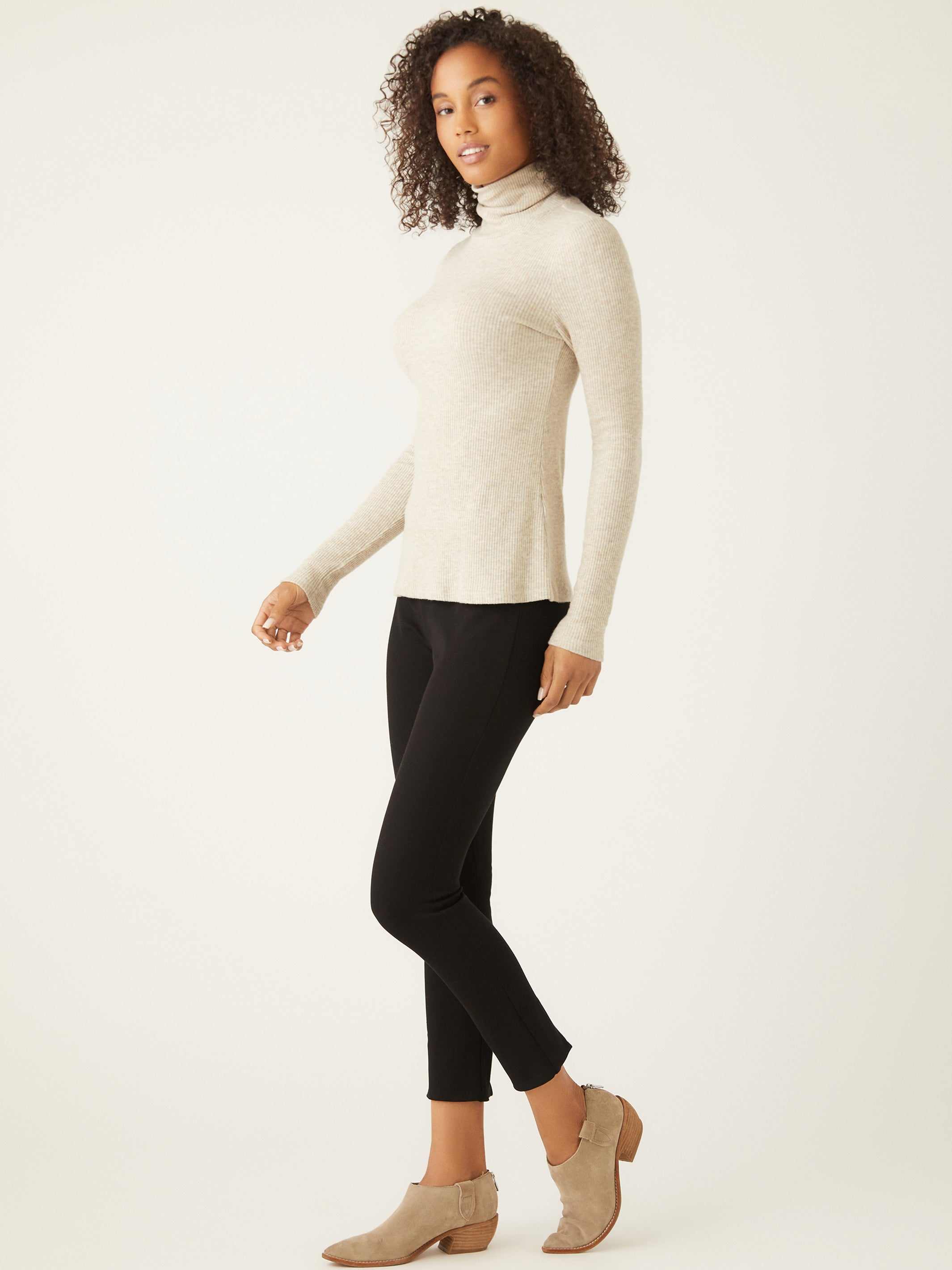 Woman wearing beige long sleeve turtleneck paired with black pants and beige ankle boots