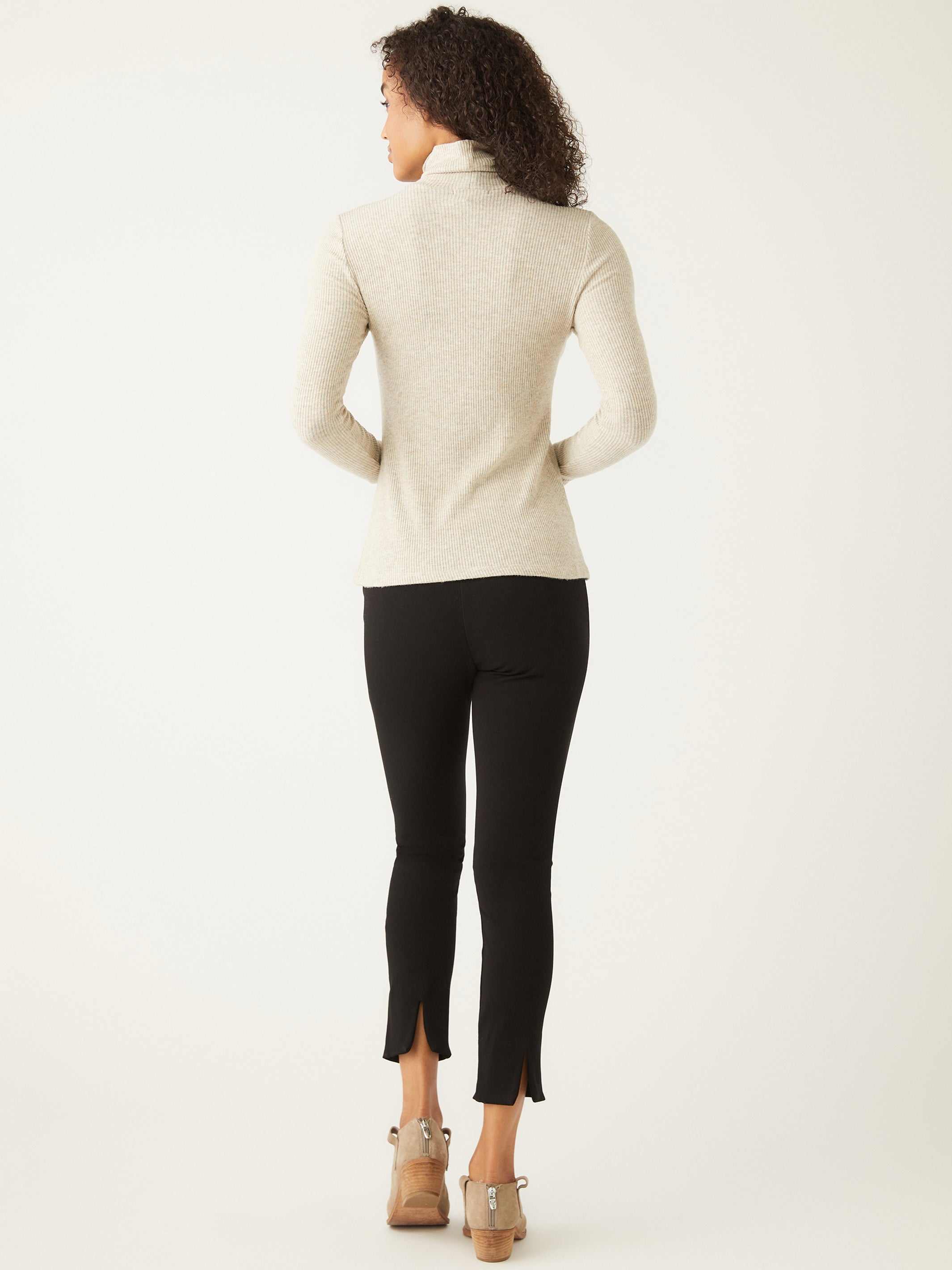 Back view of a woman wearing a beige long sleeve turtleneck and black pants with ankle slits