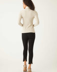 Back view of a woman wearing a beige long sleeve turtleneck and black pants with ankle slits