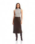 Woman wearing Brielle Midi Skirt in dark brown cupro fabric with high side slit and elastic waist, paired with grey sleeveless turtleneck and boots