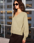 Woman wearing cozy Heather V-Neck Sweater with long raglan sleeves and ribbed trim, styled with dark skirt and sunglasses indoors.