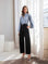 Woman wearing blue Alana Keyhole Top with knotted neckline and black wide-leg trousers in bright room
