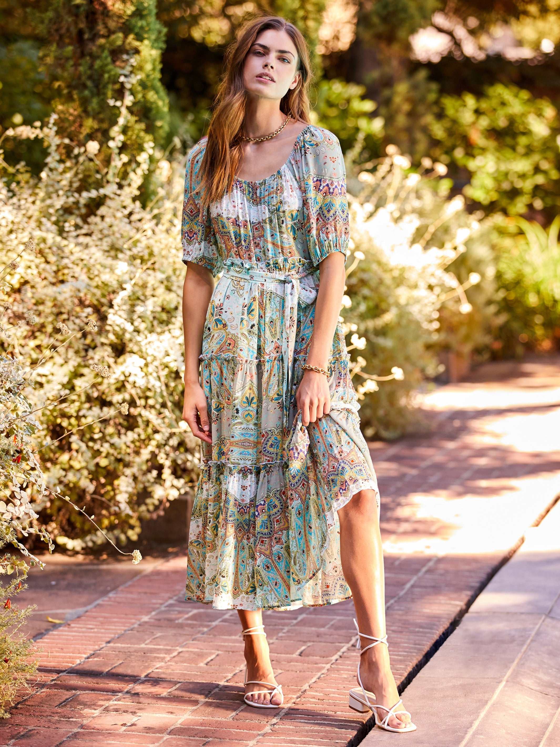 Woman wearing a colorful paisley tiered poof sleeve dress with ruffle skirt and removable waist tie outdoors