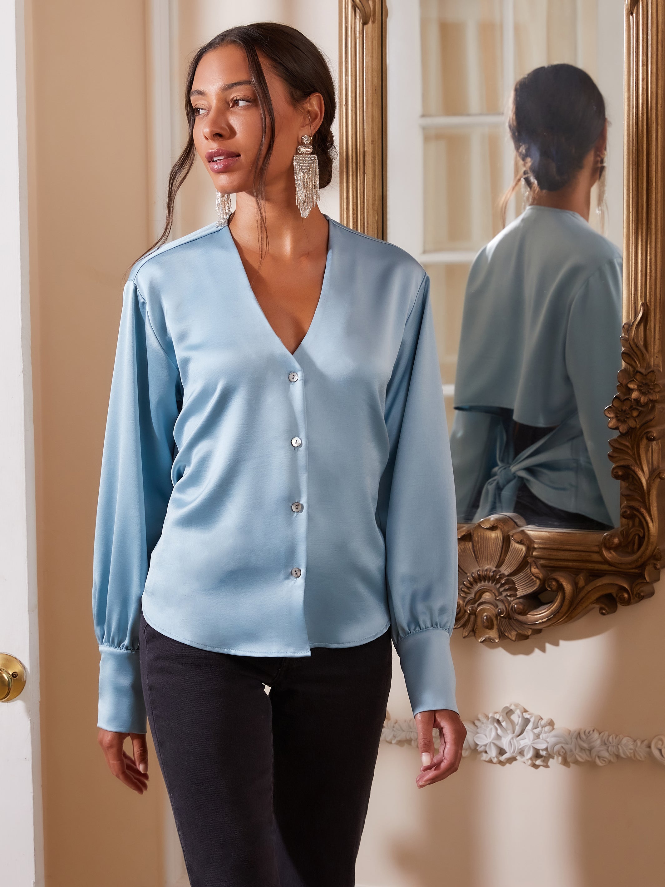 Light blue hammered satin tie back top with long cuffed sleeves and V-neck button down front worn by woman